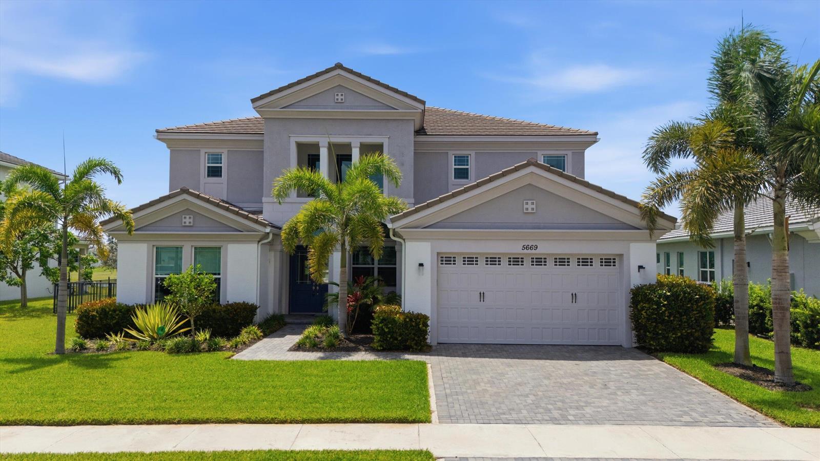 A two-story suburban house features a gray stucco exterior, a paved driveway, and palm trees — 5669 Liberty Lane, Westlake FL 33470, WESTLAKE, FL