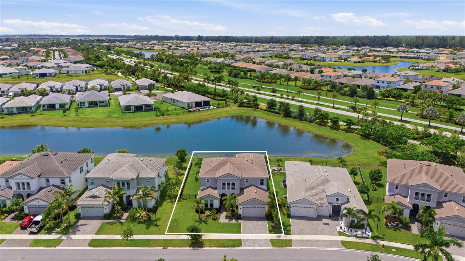 An aerial view shows a two-story suburban house with a pool, situated beside a lake — 5669 Liberty Lane, Westlake FL 33470, WESTLAKE, FL