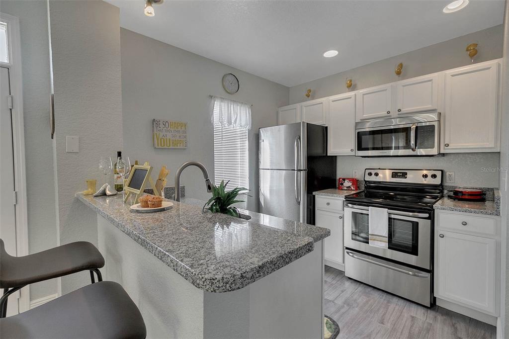 A kitchen features granite countertops, white cabinets, stainless steel appliances, and a breakfast bar — 4561 YELLOWGOLD ROAD E UNIT 102, KISSIMMEE, FL