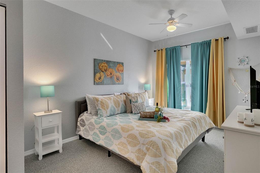 A bedroom features a bed with leaf-patterned bedding, teal and yellow curtains, and a ceiling fan — 4561 YELLOWGOLD ROAD E UNIT 102, KISSIMMEE, FL