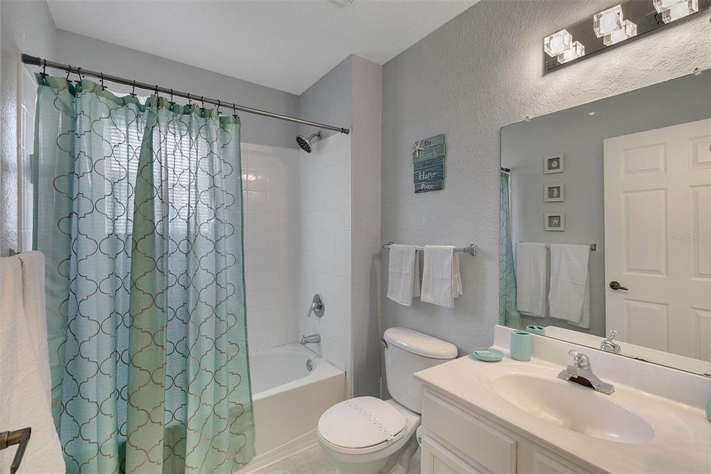 A bathroom features a white vanity, a toilet, and a shower-tub combo with a patterned curtain — 4561 YELLOWGOLD ROAD E UNIT 102, KISSIMMEE, FL