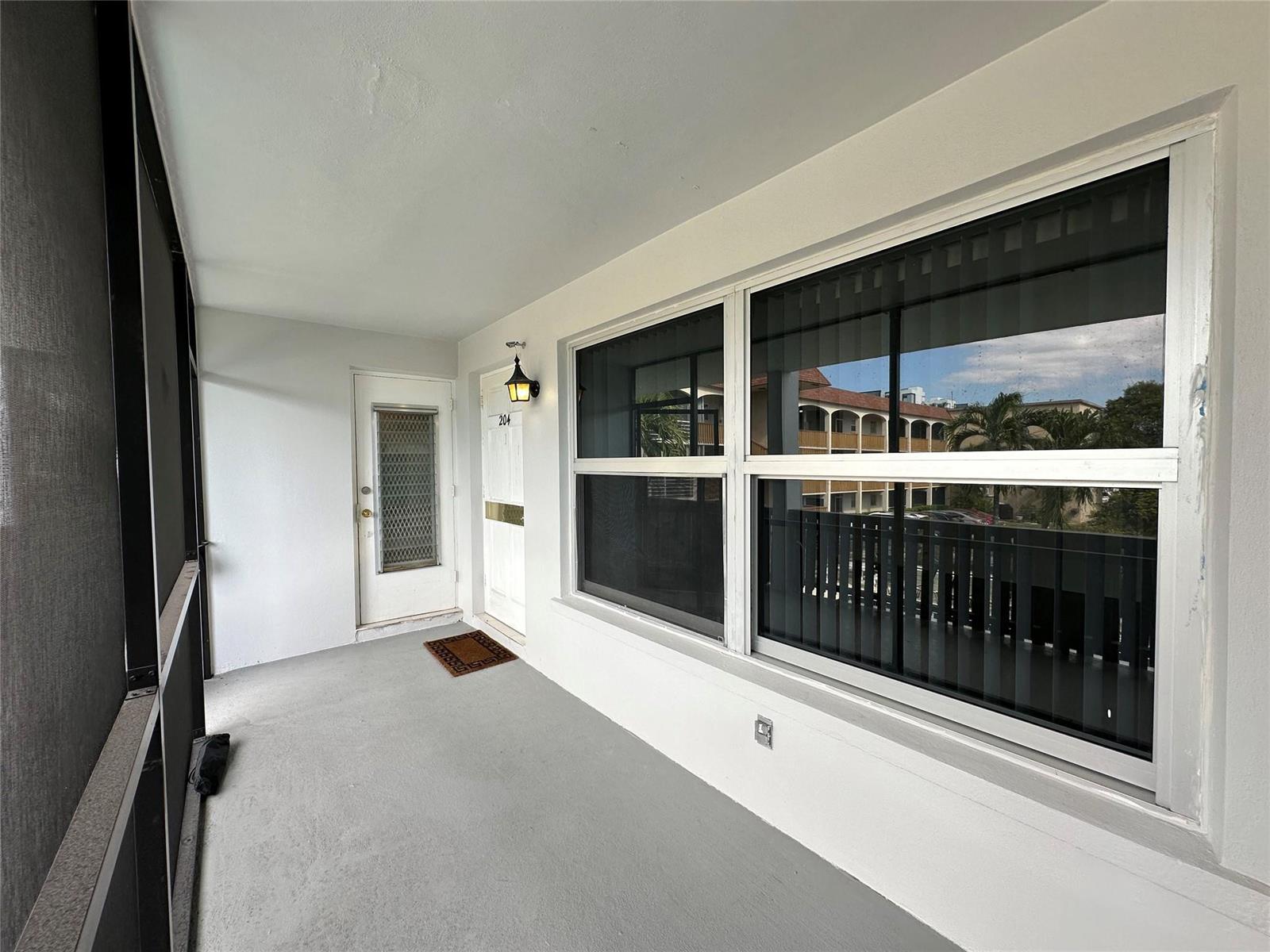 A covered balcony with gray flooring, a white door, and a large window — 651 Pine Drive, Pompano Beach FL 33060, POMPANO BEACH, FL