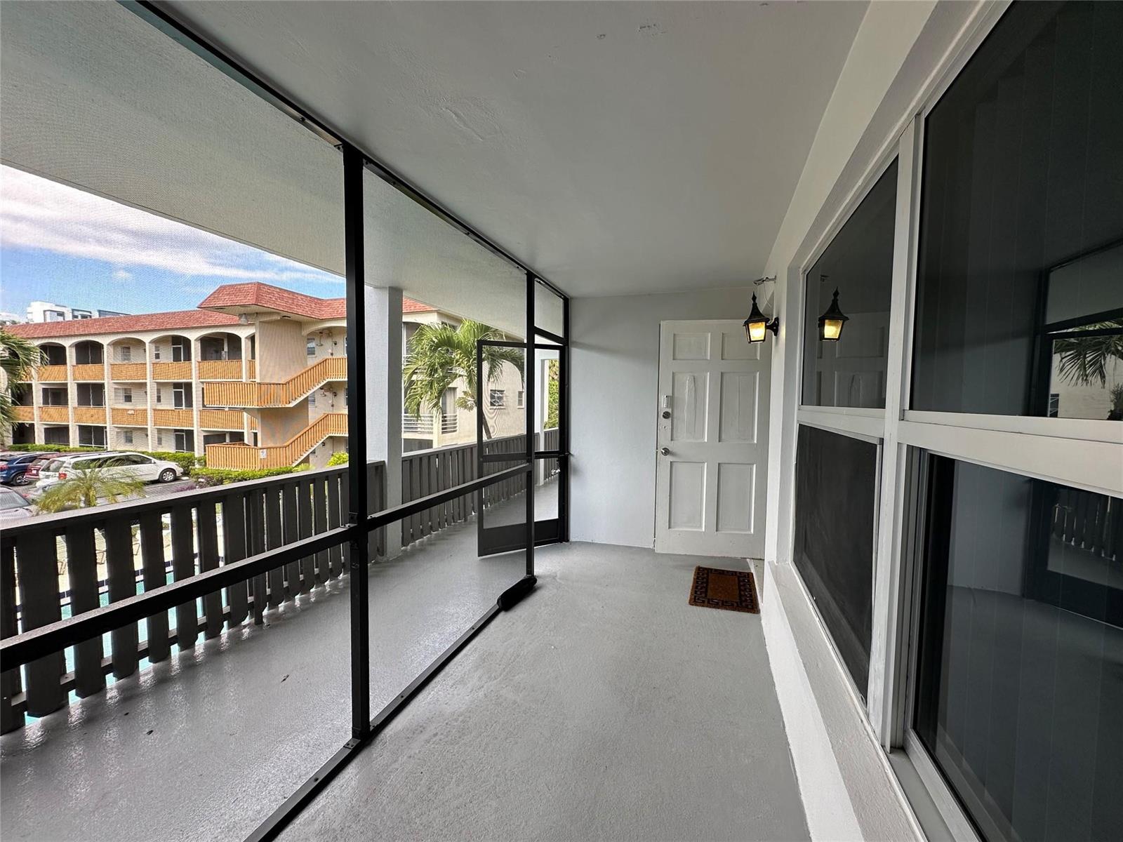 A screened-in balcony with gray flooring overlooks a parking lot and an apartment building — 651 Pine Drive, Pompano Beach FL 33060, POMPANO BEACH, FL