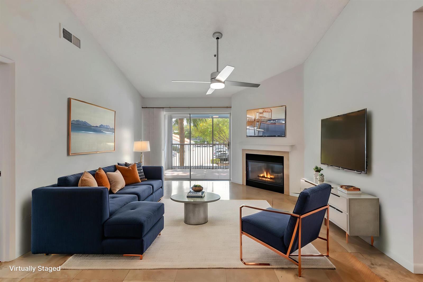 This virtually staged living room features a blue sectional, fireplace, television, and sliding glass doors — 3111 Clint Moore Road # 203, Boca Raton FL 33496, BOCA RATON, FL