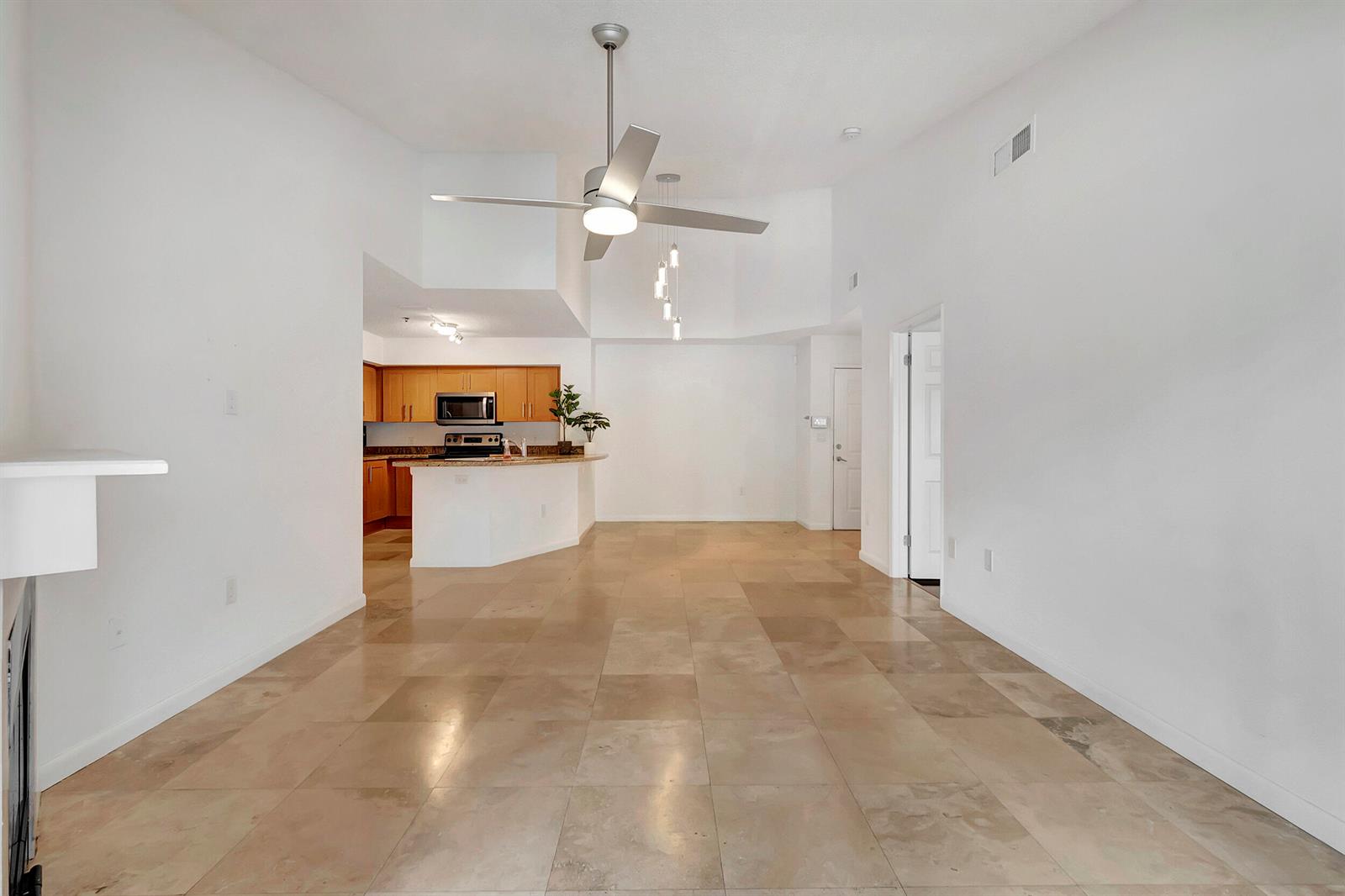 An open-concept living area features light-colored tile flooring, a ceiling fan, and a kitchen — 3111 Clint Moore Road # 203, Boca Raton FL 33496, BOCA RATON, FL