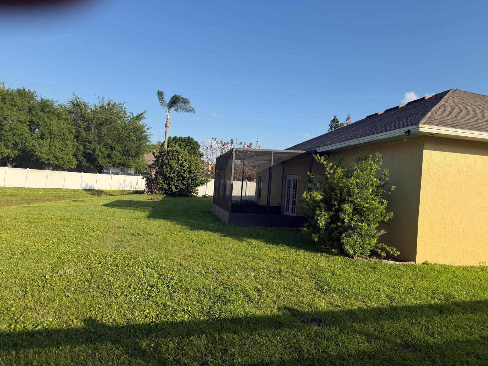 A yellow house with a screened-in patio sits in a large, grassy backyard — 123 Ruby Lake Drive, Winter Haven FL 33884, WINTER HAVEN, FL