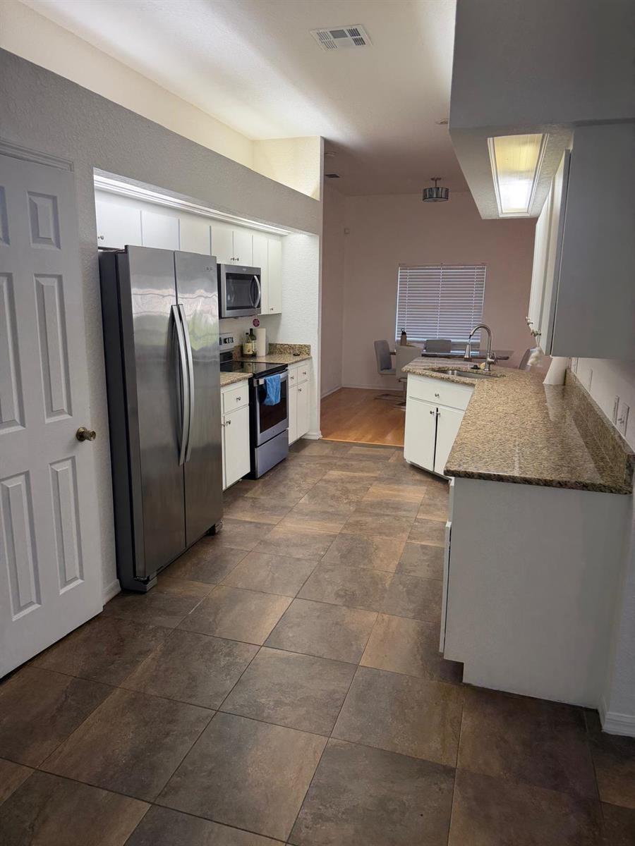 A kitchen with white cabinets, granite countertops, stainless steel appliances, and brown tile flooring — 123 Ruby Lake Drive, Winter Haven FL 33884, WINTER HAVEN, FL