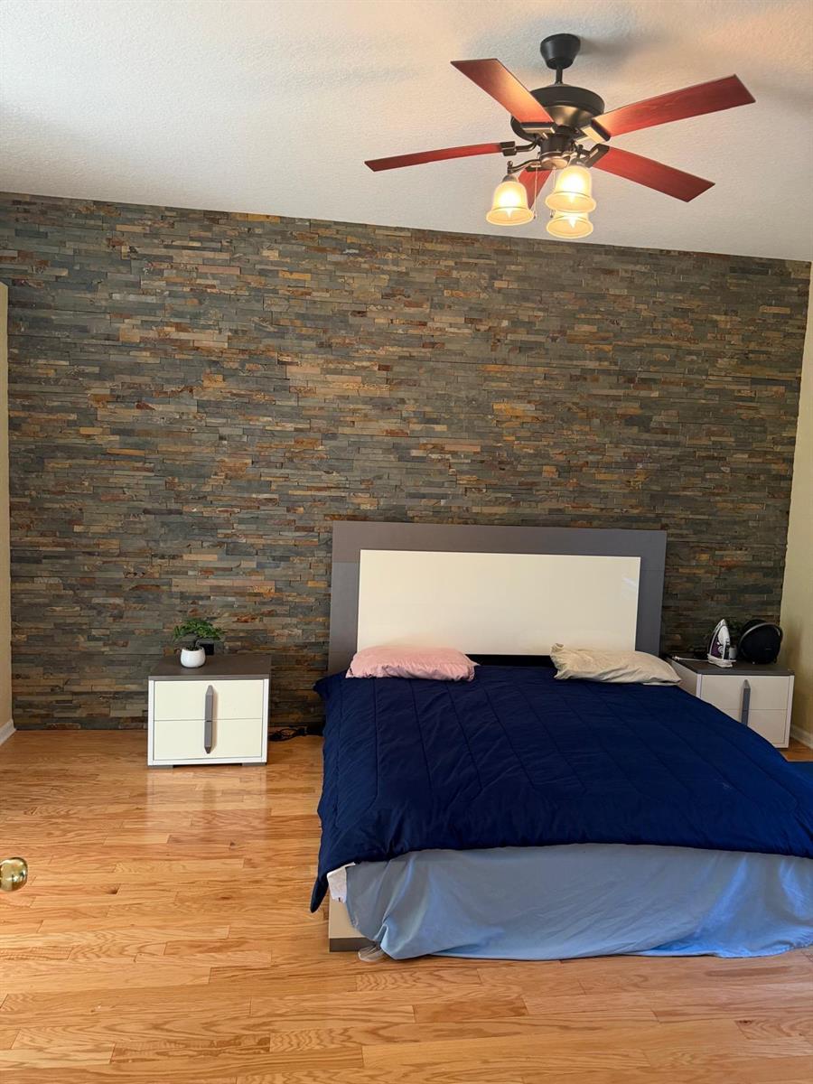 A bedroom features a stone accent wall, a modern bed frame, and hardwood flooring — 123 Ruby Lake Drive, Winter Haven FL 33884, WINTER HAVEN, FL