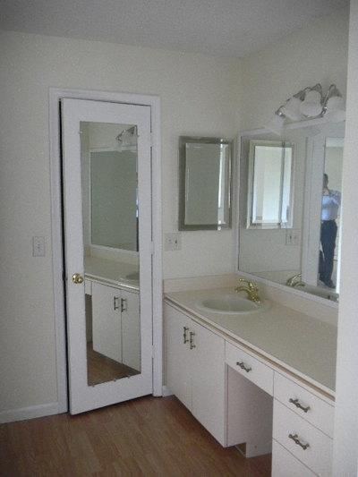A bathroom vanity with white cabinets, a mirror, and a full-length mirror on the door — 1561 NW 20th Avenue # 101, Delray Beach FL 33445, DELRAY BEACH, FL