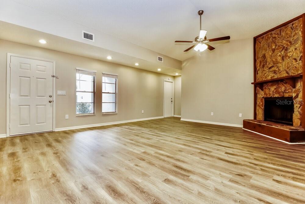 A living room with light wood-look flooring, a stone fireplace, and a ceiling fan — 1828 CRAVEN DRIVE, SEFFNER, FL