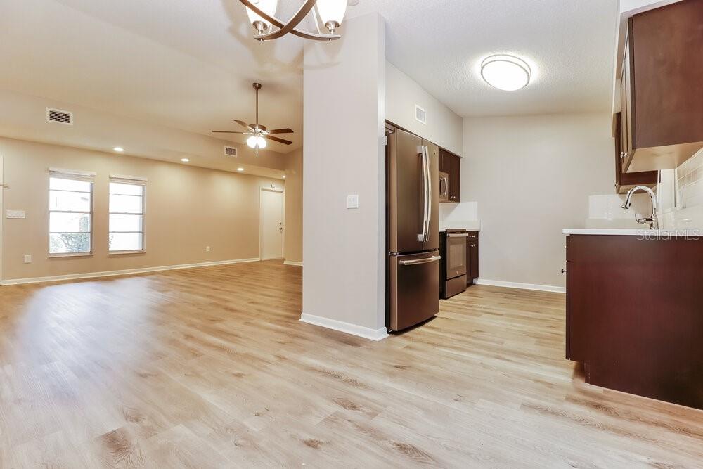 A kitchen with stainless steel appliances and wood-look flooring opens into a spacious living area — 1828 CRAVEN DRIVE, SEFFNER, FL