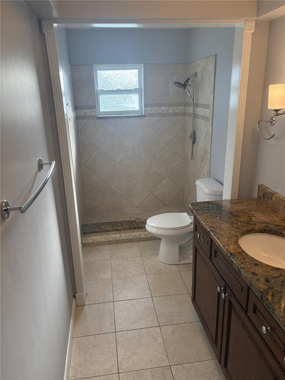 A bathroom features a tiled walk-in shower, a toilet, and a granite-topped vanity — 5784 BAY PINES LAKES BOULEVARD, ST PETERSBURG, FL