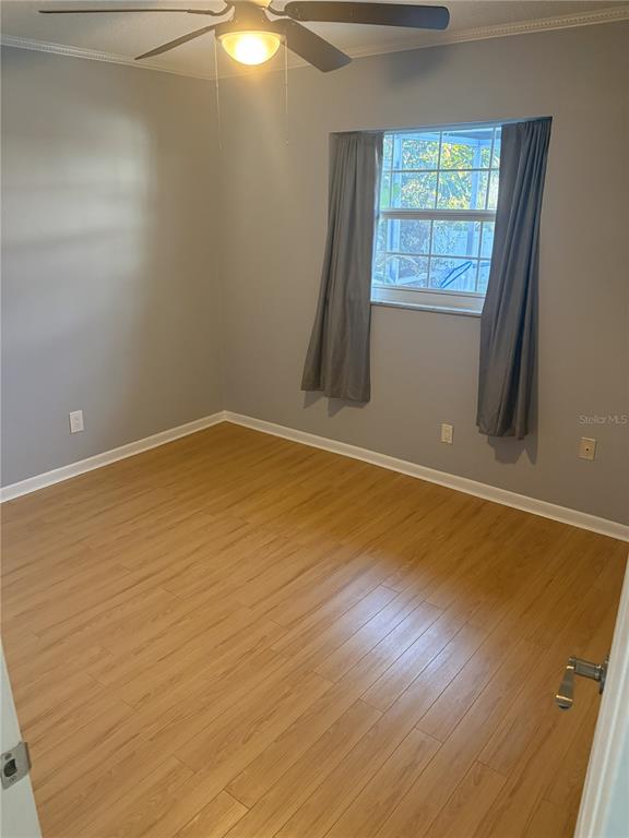 An empty bedroom features light wood-look flooring, gray walls, a ceiling fan, and a window — 5784 BAY PINES LAKES BOULEVARD, ST PETERSBURG, FL
