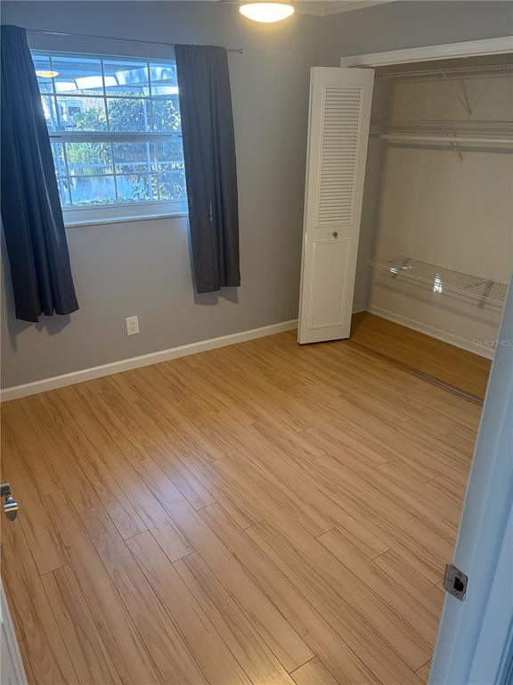 A bedroom with light wood-look flooring, gray walls, a window with curtains, and a closet — 5784 BAY PINES LAKES BOULEVARD, ST PETERSBURG, FL