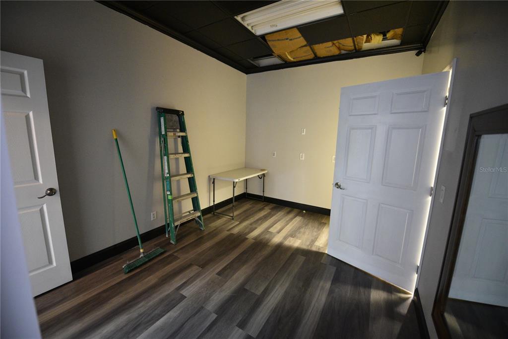 An empty room features wood-look flooring, white walls, a black ceiling, and a folding table — 5124 US HIGHWAY 19, NEW PORT RICHEY, FL