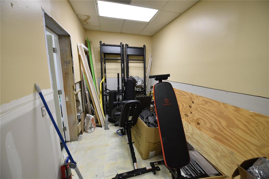 A small, unfinished room contains exercise equipment, construction materials, and a partially installed doorway — 5124 US HIGHWAY 19, NEW PORT RICHEY, FL