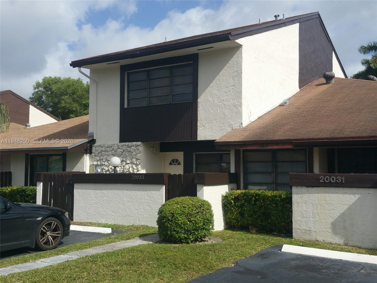 A two-story townhouse with a brown shingled roof, stucco exterior, and a private fenced patio — 20033 NE 2nd Pl, Miami FL 33179, MIAMI, FL