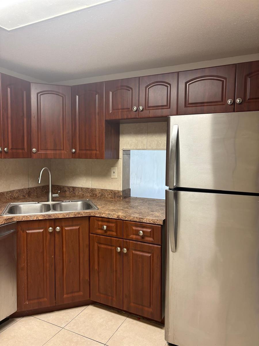 A kitchen features dark wood cabinets, a stainless steel refrigerator, and a double-basin sink — 1700 NW 58th Terrace # 1b, Sunrise FL 33313, SUNRISE, FL