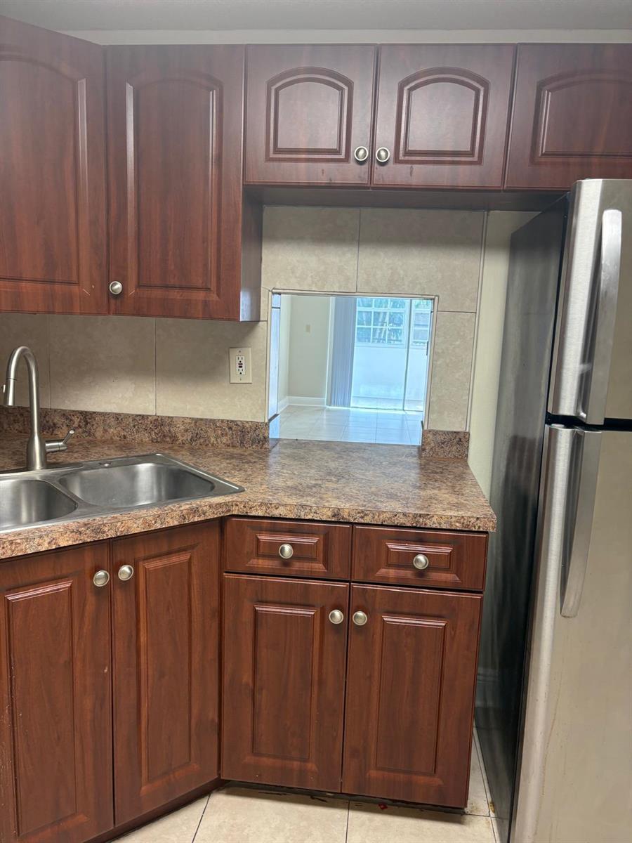 A kitchen features dark wood cabinets, laminate countertops, a stainless steel sink, and a pass-through window — 1700 NW 58th Terrace # 1b, Sunrise FL 33313, SUNRISE, FL