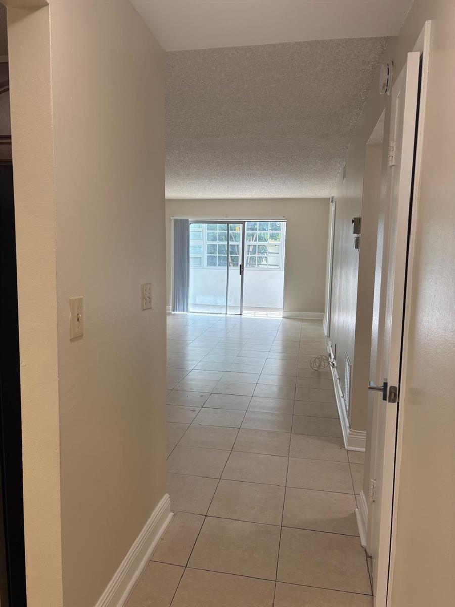 A view from a hallway looking into a living area with tile floors and sliding doors — 1700 NW 58th Terrace # 1b, Sunrise FL 33313, SUNRISE, FL