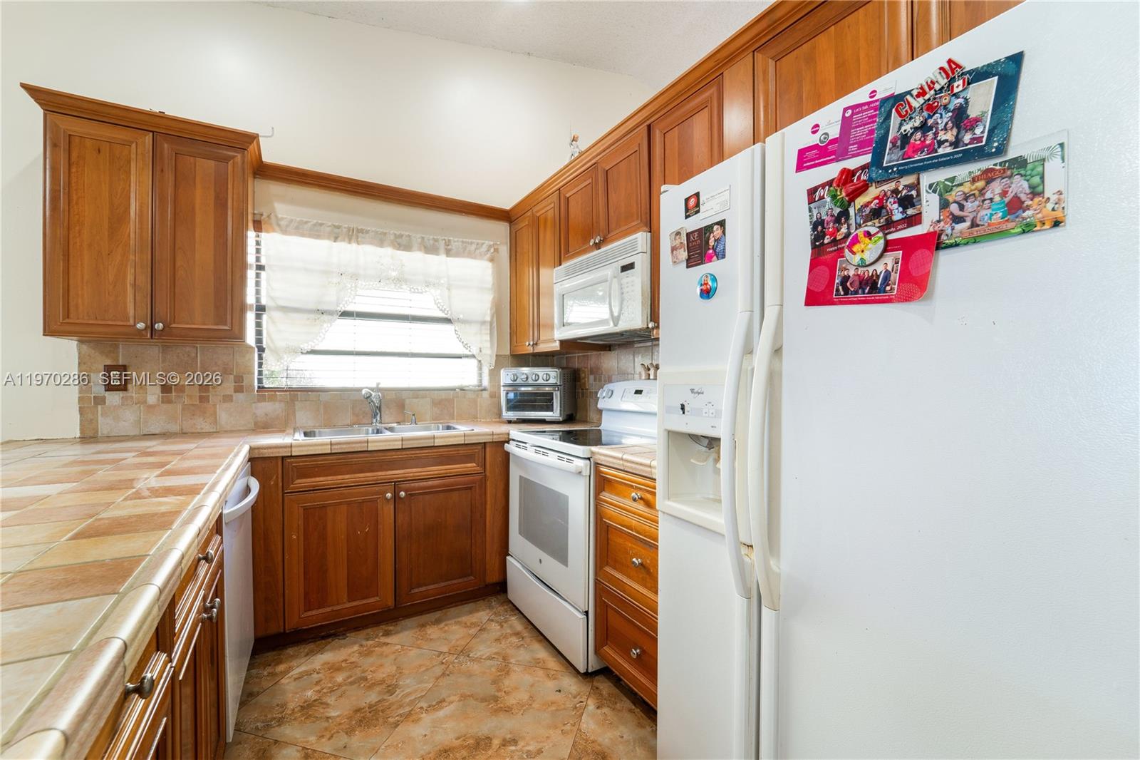A kitchen features wood cabinets, tile countertops, a white refrigerator, and a tiled floor — 14526 SW 106th Ter, Miami FL 33186, MIAMI, FL