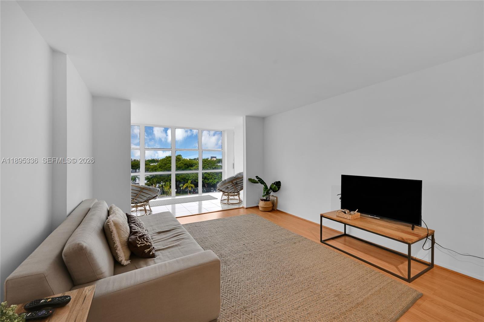 A living room features a sofa, television on a stand, and floor-to-ceiling windows — 800 Parkview Dr # 605, Hallandale Beach FL 33009, HALLANDALE BEACH, FL