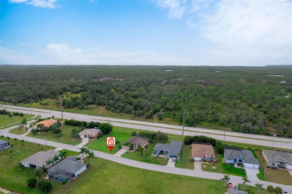 An aerial view shows a suburban street with houses and a large wooded area nearby — 7353 N SEAGRAPE ROAD, PUNTA GORDA, FL