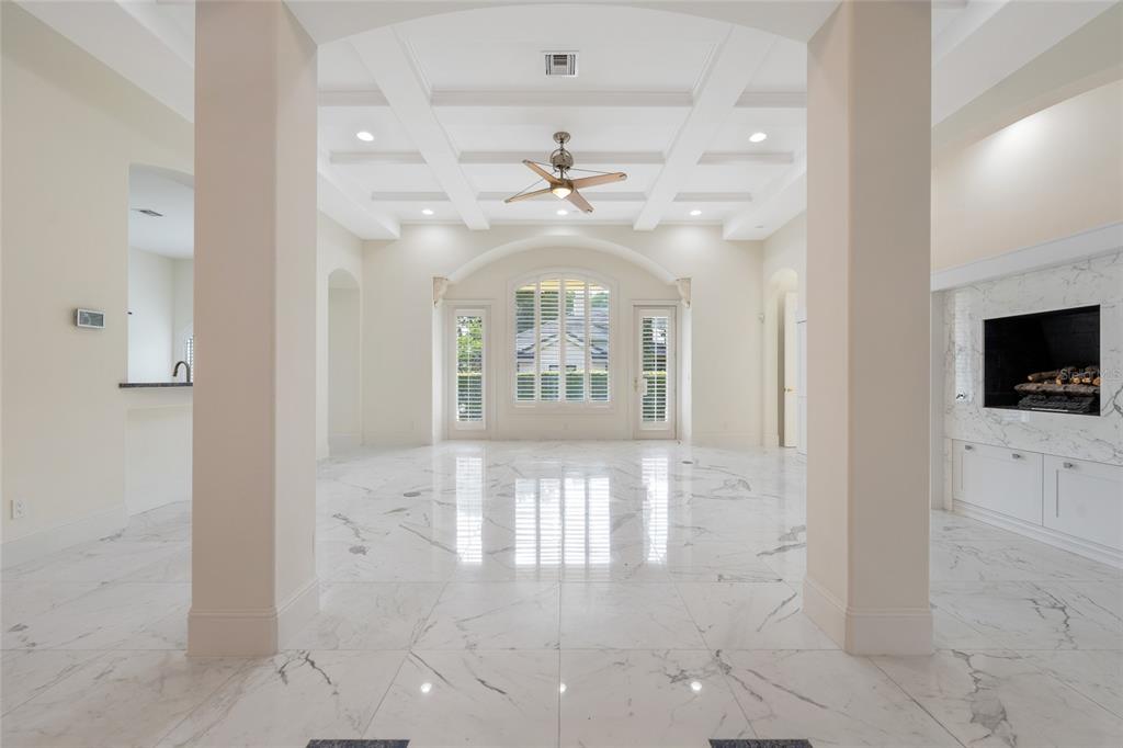 A bright, open living room features white marble floors, a coffered ceiling, and a fireplace — 9701 LAKE ISLEWORTH COURT, WINDERMERE, FL