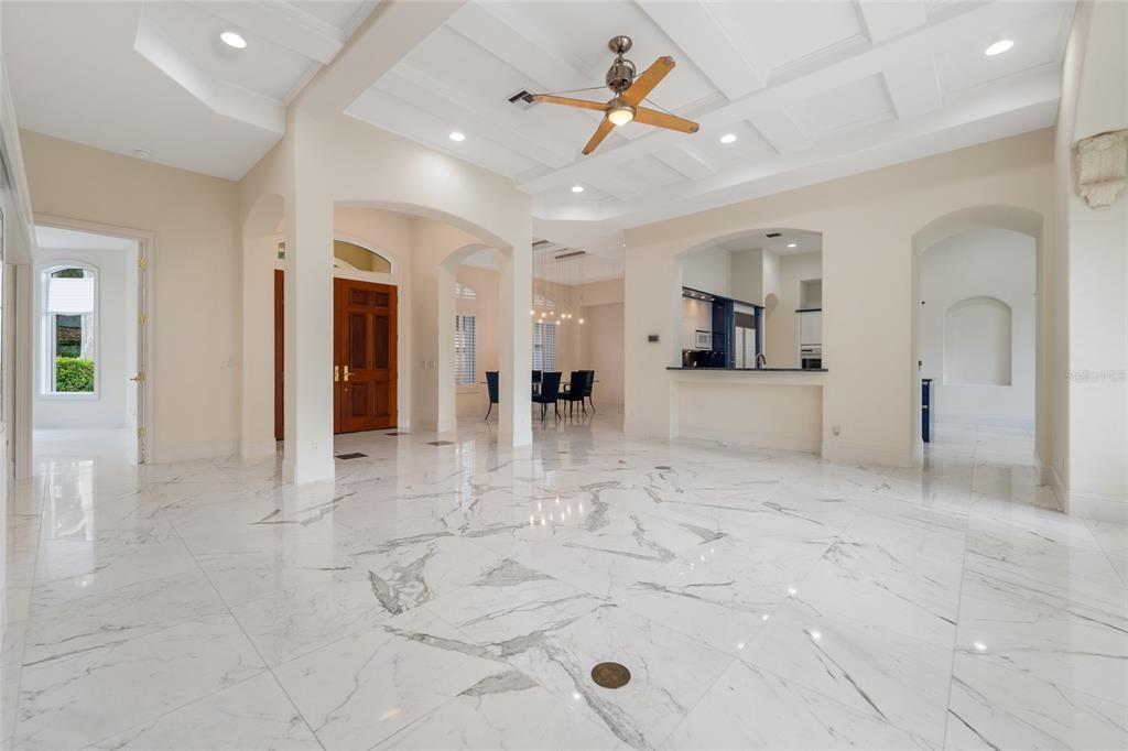 A spacious living area with white marble floors, a coffered ceiling, and an open kitchen — 9701 LAKE ISLEWORTH COURT, WINDERMERE, FL