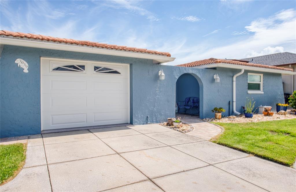 A blue house exterior features a white garage door, a tiled roof, and an arched entryway — 7039 SOUTHWIND DRIVE, HUDSON, FL