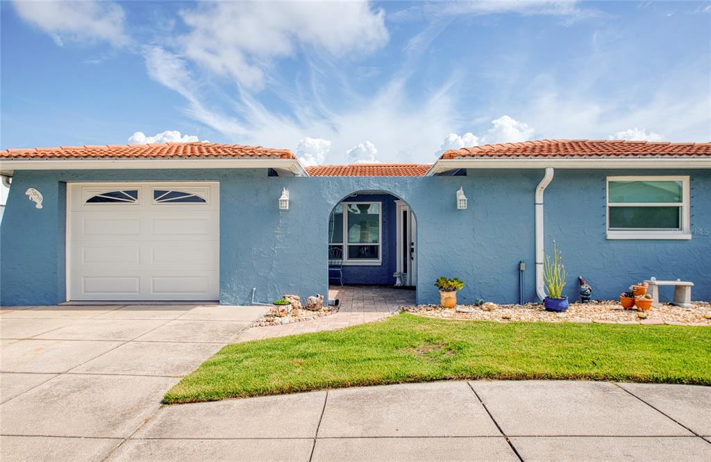 A blue single-story house with a white garage door, arched entryway, and terracotta roof tiles — 7039 SOUTHWIND DRIVE, HUDSON, FL