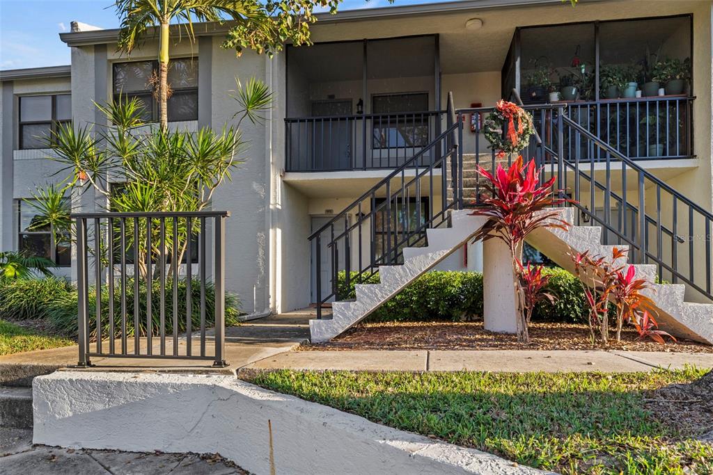 A two-story apartment building exterior features a concrete staircase leading to an upper-level balcony — 1918 PELICAN LANDING BOULEVARD UNIT 1125, CLEARWATER, FL