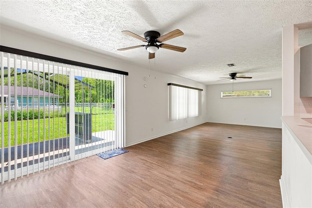 An open living area features wood-look flooring, two ceiling fans, and sliding glass patio doors — 1009 TULANE TERRACE, INVERNESS, FL