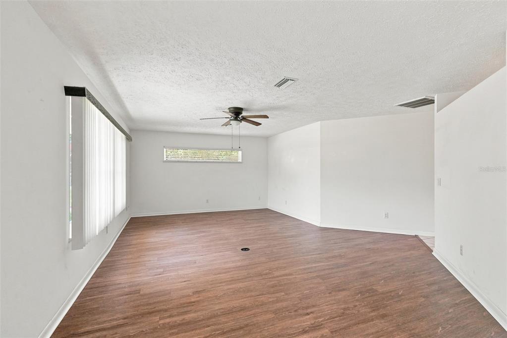 An empty room with wood-look flooring, white walls, a ceiling fan, and vertical window blinds — 1009 TULANE TERRACE, INVERNESS, FL