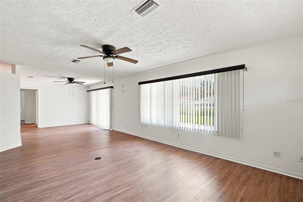 An empty living room features wood-look flooring, white walls, two ceiling fans, and vertical blinds — 1009 TULANE TERRACE, INVERNESS, FL