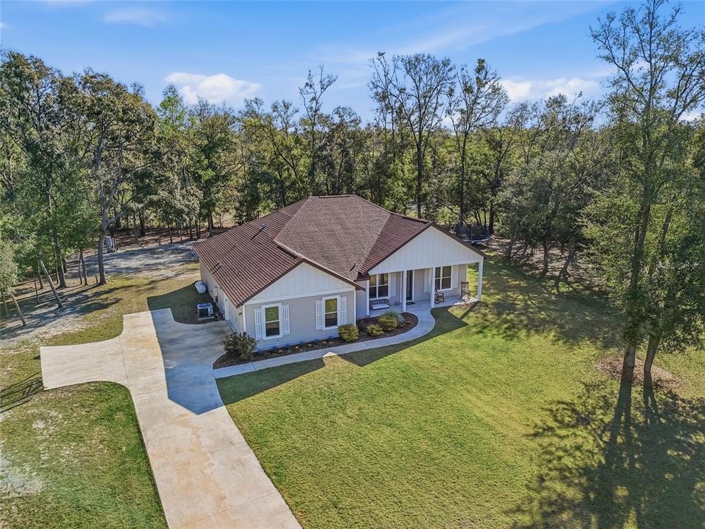 An aerial view shows a single-story house with a concrete driveway and wooded surroundings — 8920 NE 8TH PLACE, HIGH SPRINGS, FL