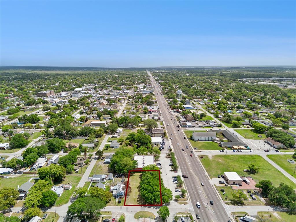 An aerial view shows a rectangular, tree-covered vacant lot outlined in red along a road — 1215 WISCONSIN AVENUE, ST CLOUD, FL