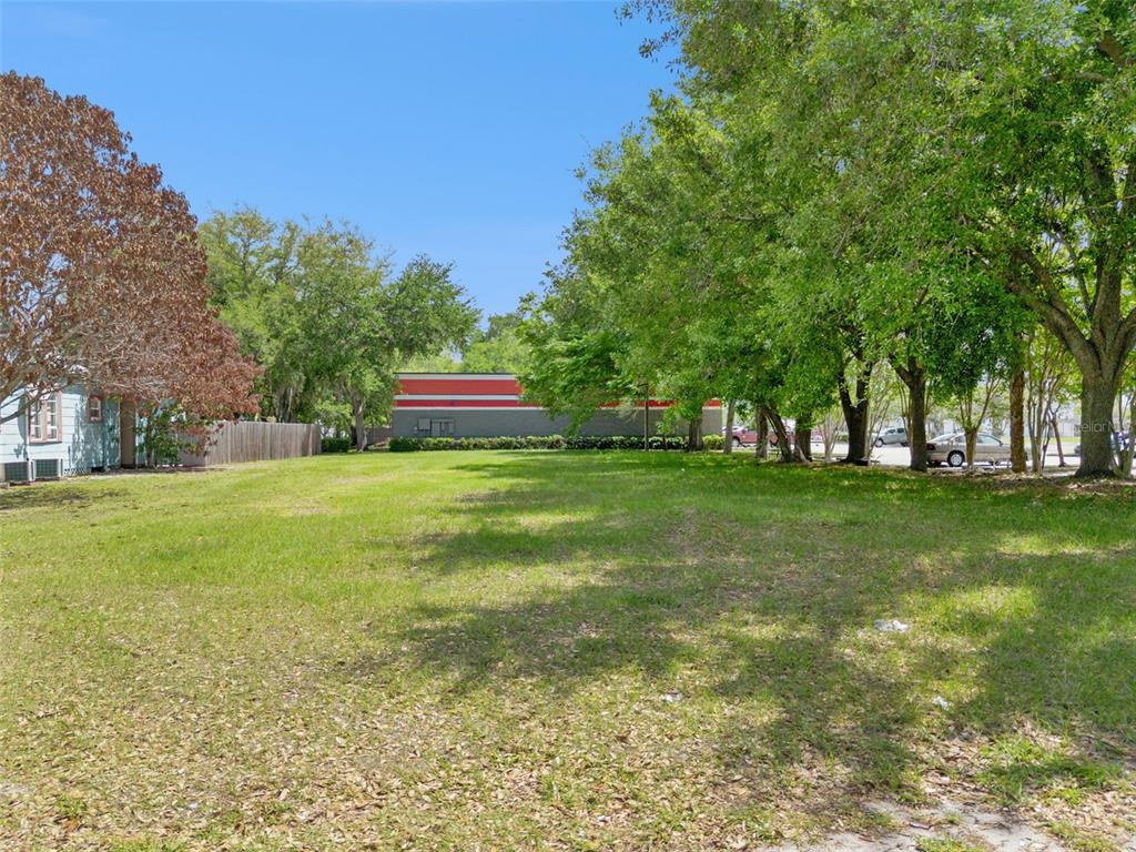 A vacant, grassy lot is bordered by trees and a neighboring building under a blue sky — 1215 WISCONSIN AVENUE, ST CLOUD, FL