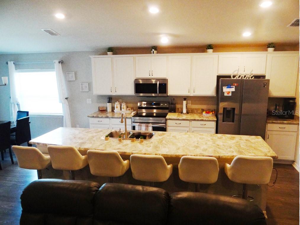 A kitchen features white cabinets, a large island with bar seating, and stainless steel appliances — 621 VITTORIO DRIVE, WINTER HAVEN, FL