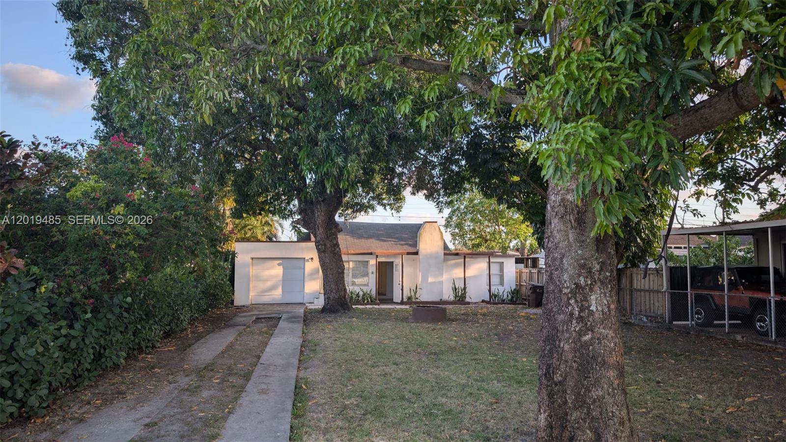 A single-story house with a garage and driveway sits behind large trees in a yard — 76 W 14th St, Hialeah FL 33010, HIALEAH, FL