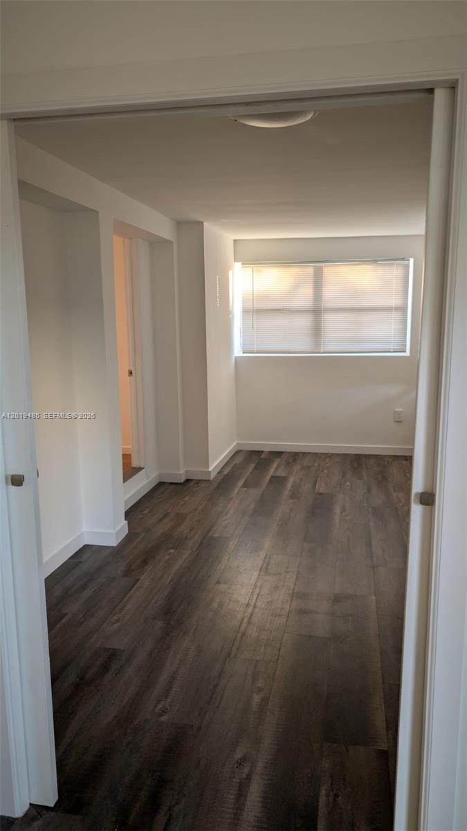 An empty room features dark wood-look flooring, white walls, and a window with blinds — 76 W 14th St, Hialeah FL 33010, HIALEAH, FL