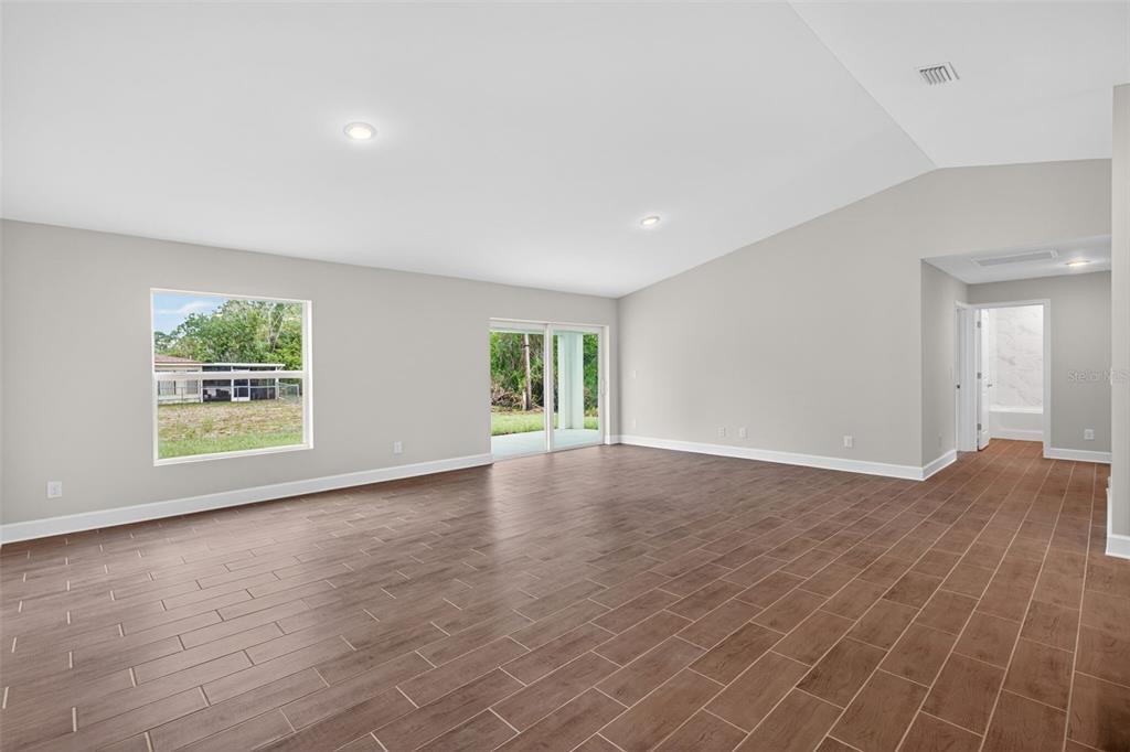 A living and dining room with gray furniture, wood-look tile floors, and a vaulted ceiling — 23447 BEATRICE AVENUE, PORT CHARLOTTE, FL