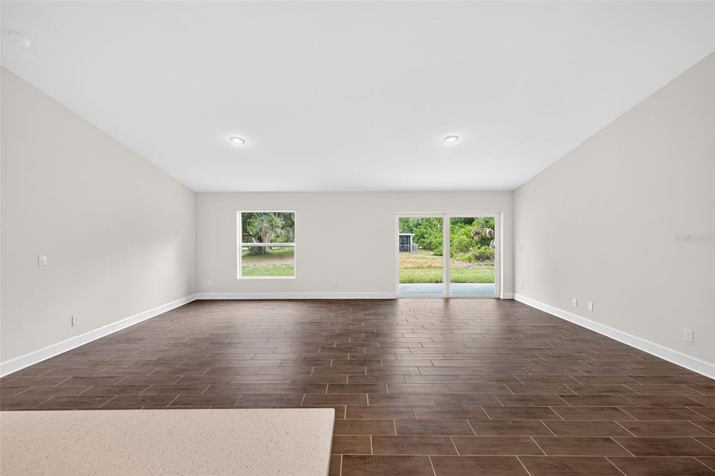A spacious living room features light gray walls, wood-look tile flooring, and a sliding glass door — 23447 BEATRICE AVENUE, PORT CHARLOTTE, FL