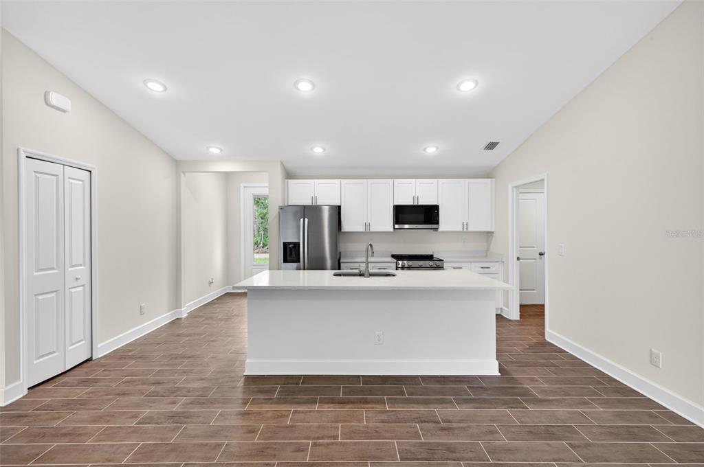 An empty living room features light-colored walls, dark wood-look tile flooring, and sliding glass doors — 23447 BEATRICE AVENUE, PORT CHARLOTTE, FL