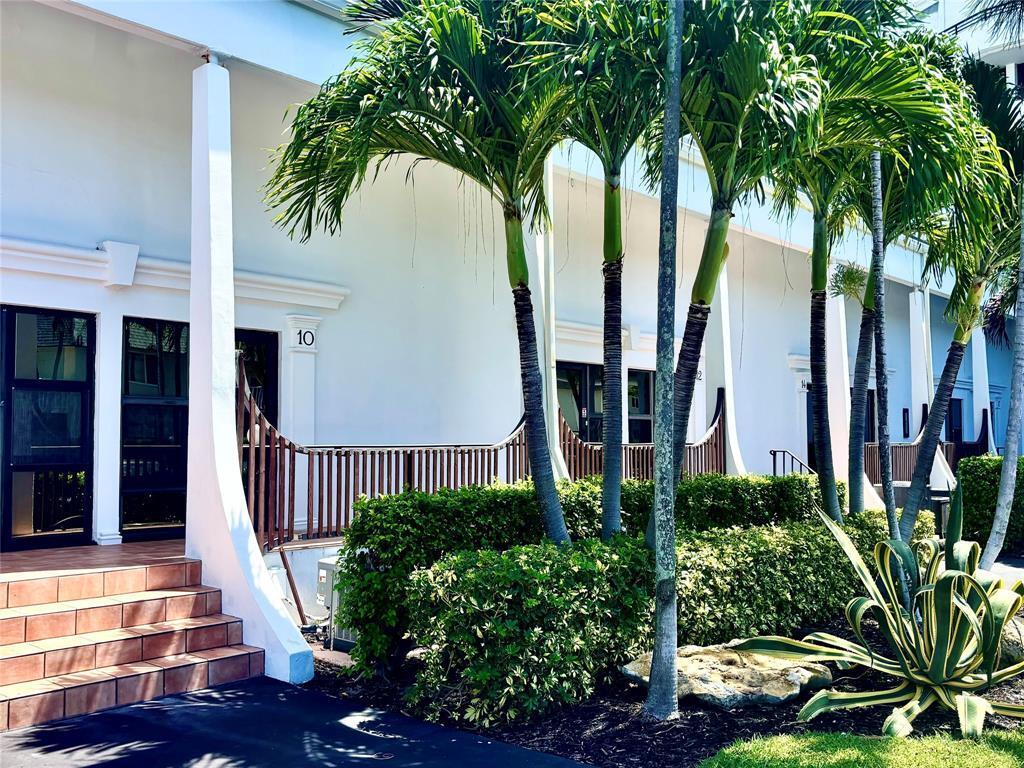 A white building exterior features a tiled staircase, palm trees, and a wooden balcony railing — 3589 S Ocean Boulevard # 10, South Palm Beach FL 33480, SOUTH PALM BEACH, FL
