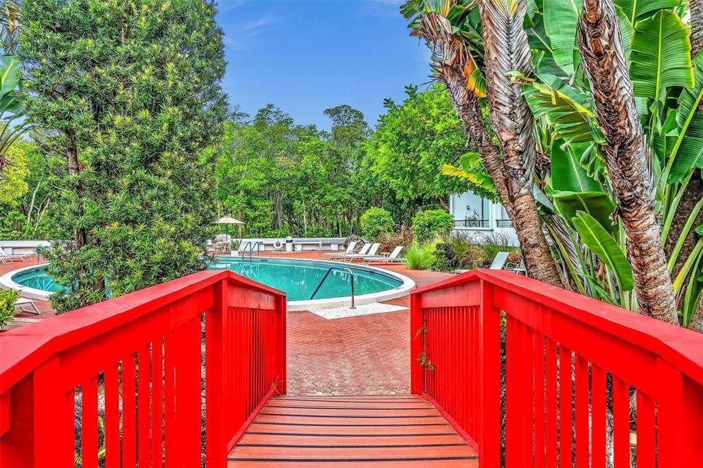 A red wooden bridge leads to a curved swimming pool surrounded by trees and landscaping — 3589 S Ocean Boulevard # 10, South Palm Beach FL 33480, SOUTH PALM BEACH, FL