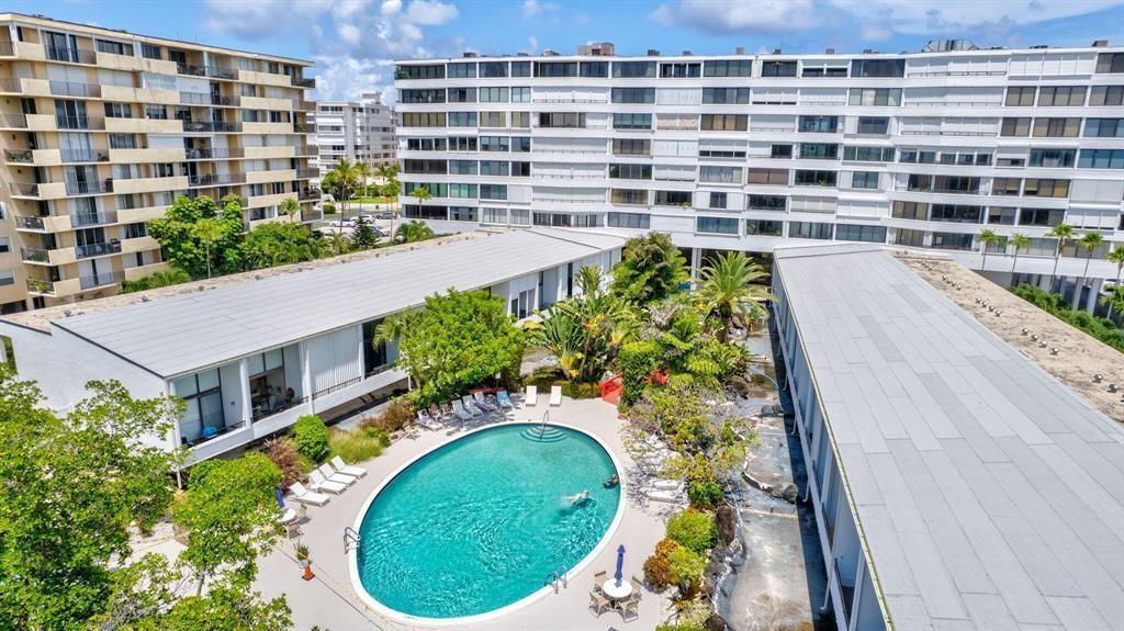 An aerial view shows a swimming pool nestled between two low-rise buildings and a high-rise — 3589 S Ocean Boulevard # 10, South Palm Beach FL 33480, SOUTH PALM BEACH, FL