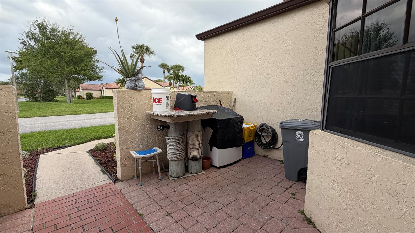A paved patio area features a small stone-topped table, a trash bin, and a grill — 8232 Waterline Drive, Boynton Beach FL 33472, BOYNTON BEACH, FL