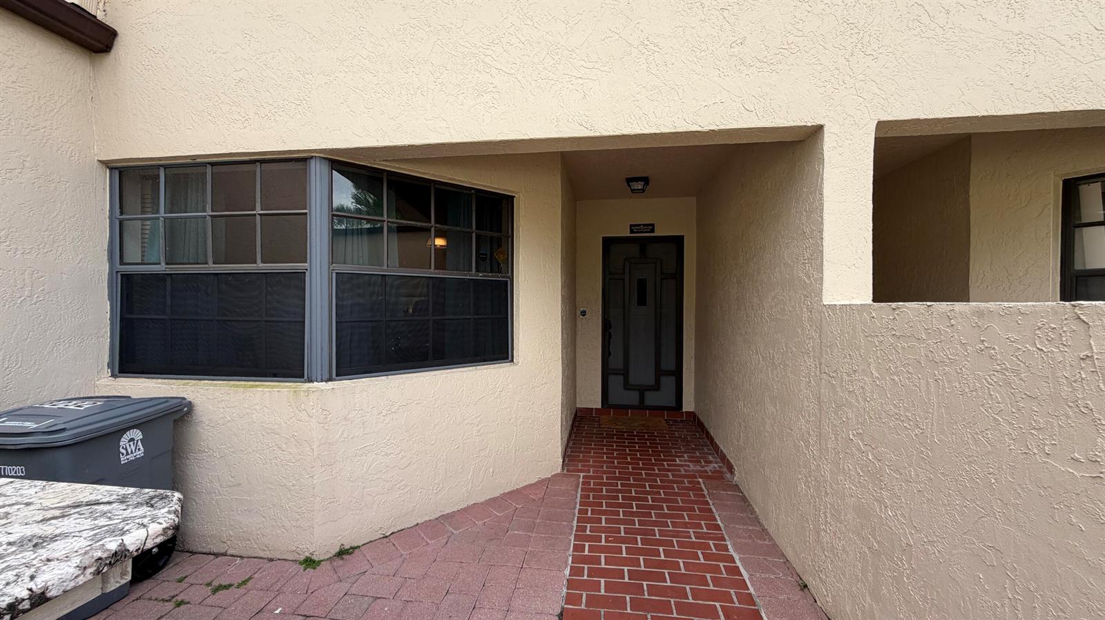 A tan stucco building exterior features a brick walkway leading to a dark front door — 8232 Waterline Drive, Boynton Beach FL 33472, BOYNTON BEACH, FL