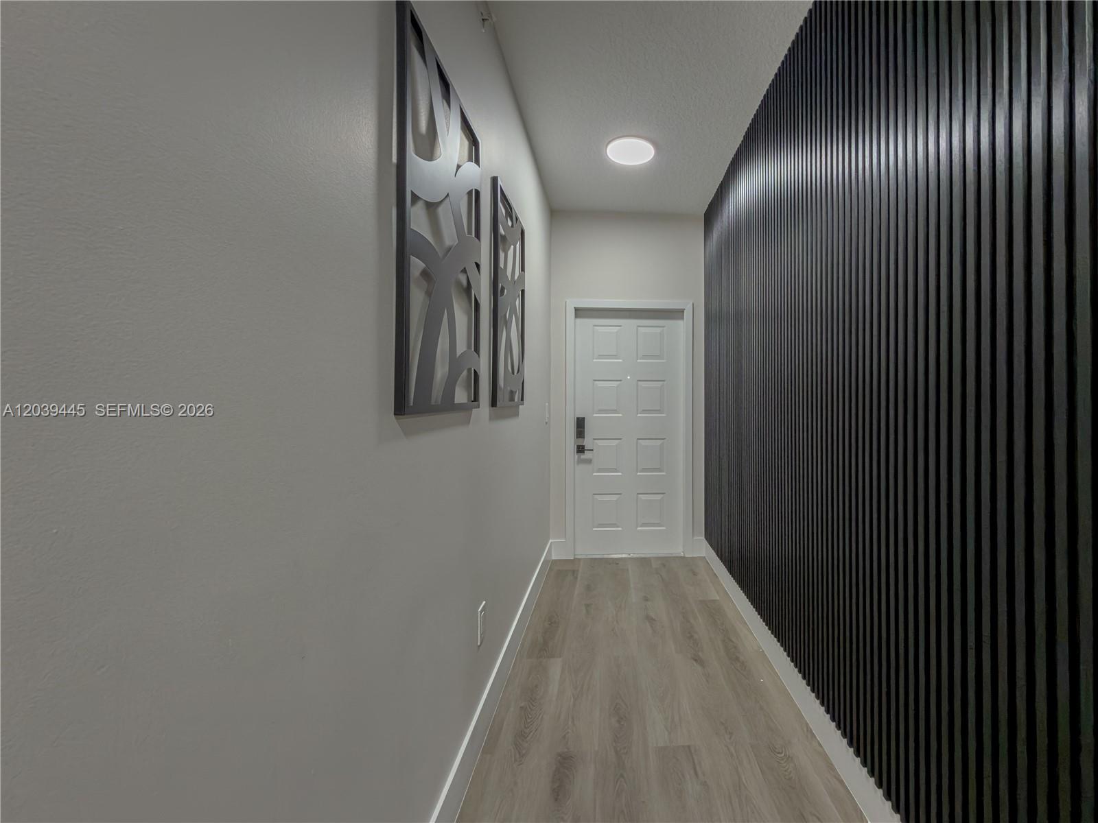 A hallway features light wood-look flooring, a white door, and a black slatted accent wall — 10750 NW 66th St # 504, Doral FL 33178, DORAL, FL